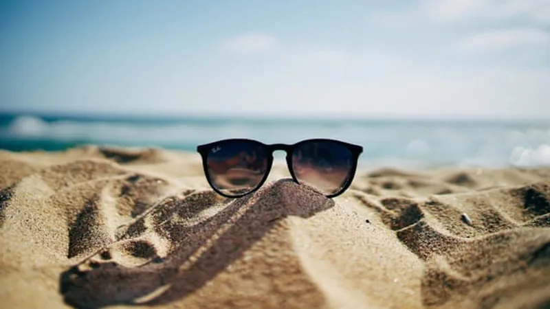 Sunglasses resting on beach sand, summer banner shown to subscribers in warm, sunny locations